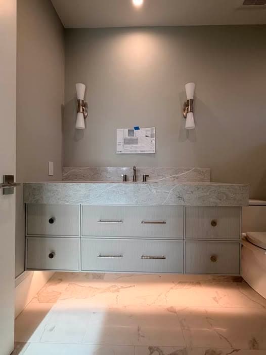 Floating bathroom vanity with fluted white drawer fronts, brushed nickel handles and a stone top with a matching splashback